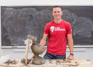 A man in a red t-shirt stands in front of a clay work table
