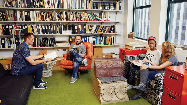 Four people sit in a louge surrounded by books. 