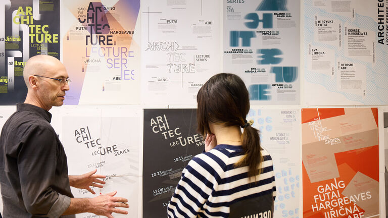 A student and a faculty member talk next to a wall with posters.
