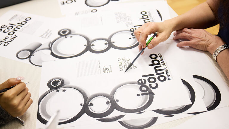 Two students sitting at a table with pens, looking at an array of documents.