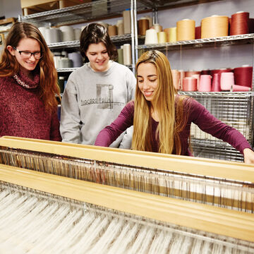 Three students working at a loom.