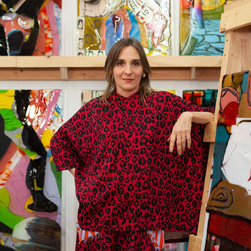 An artist stands in front of brightly painted canvases