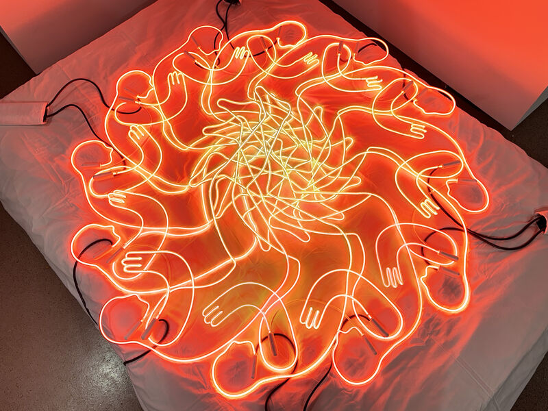 A neon sign of overlapping figures laying on a mattress