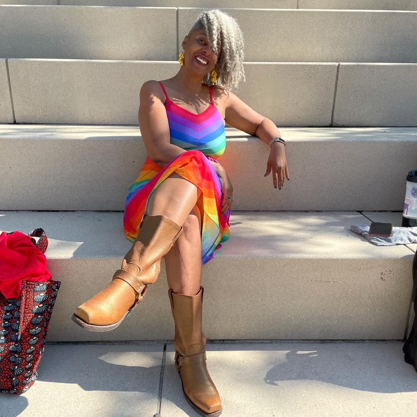 A person in a rainbow dress sits on stone steps