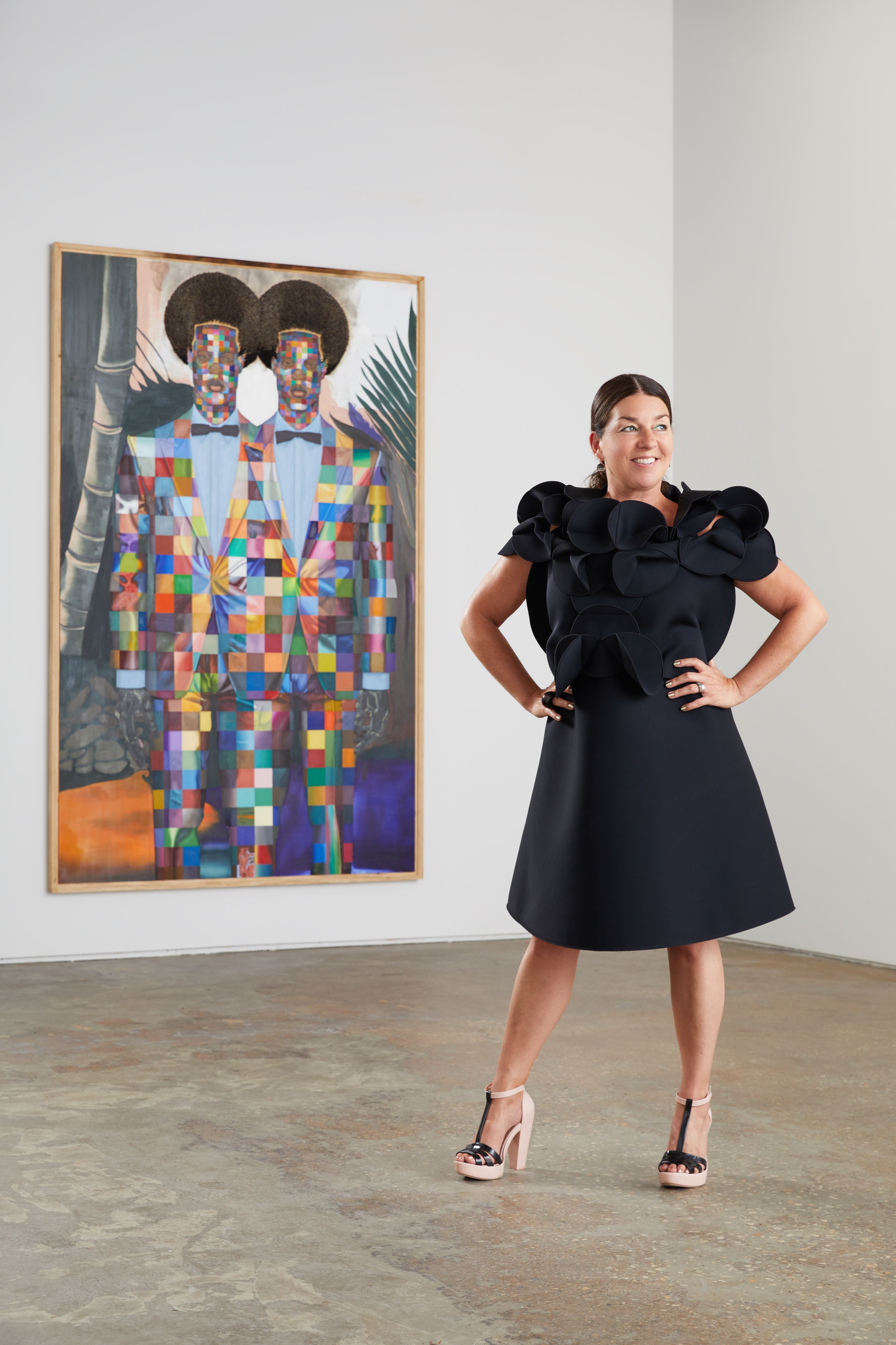 A curator in a black dress stands in front of a painting