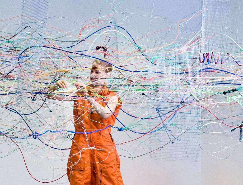 An artist stands amidst static, colored wires