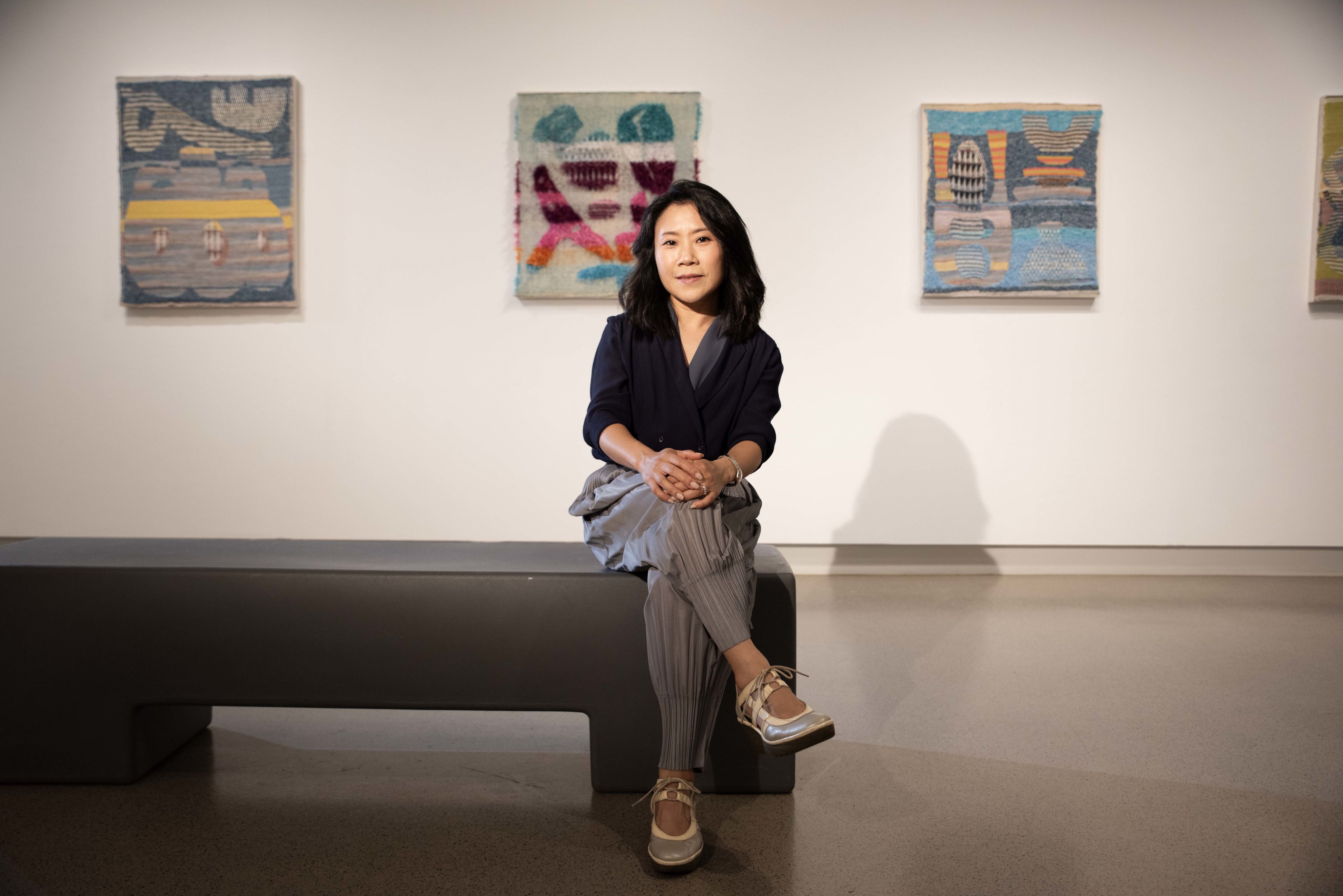 A woman sits on a concrete bench in a modern gallery space