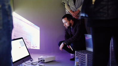 A person crouching down to look at a monitor on the floor. 