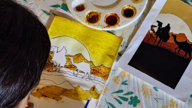  A young girl painting a desert landscape with spices on a table, focused and creative