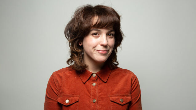 An arts administrator in a red shirt poses in front of a white background