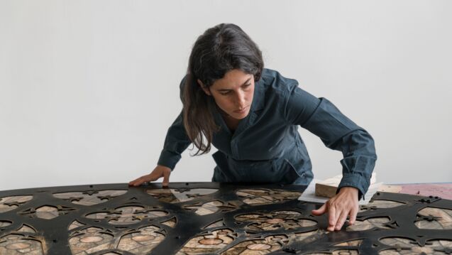 A woman with brown hair stands over an installation in front of a white background