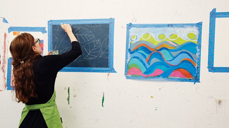 A person drawing on a piece of paper taped up to the wall.