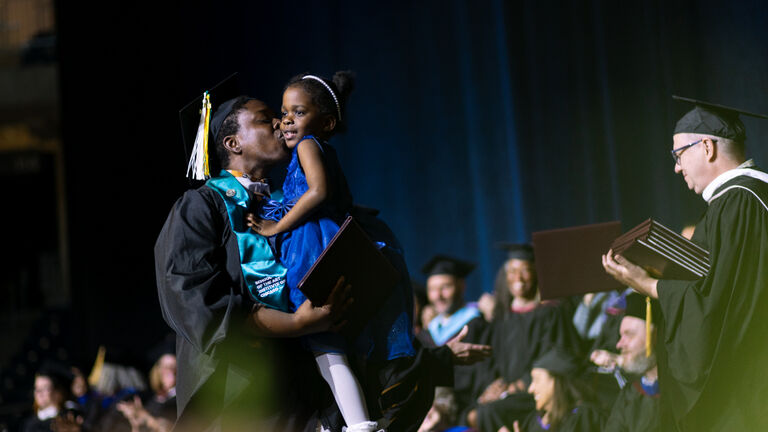 A student kisses their child when crossing the stage