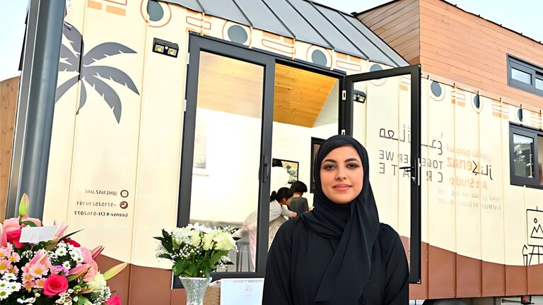 SAIC alum Ghaleya Almansoori standing in front of mobile studio Kenaz.