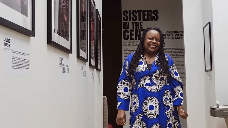 Dr. Yvonne Welbon at Sisters in Cinema Arts Center, with a background showcasing posters of films.
