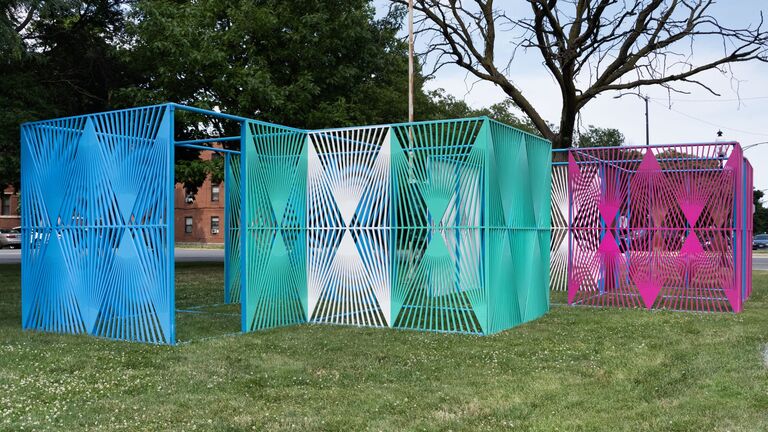 A collection of vibrant metal breezeways, Soto's "Graft" series arranged on a grassy surface, showcasing a variety of colors and designs.