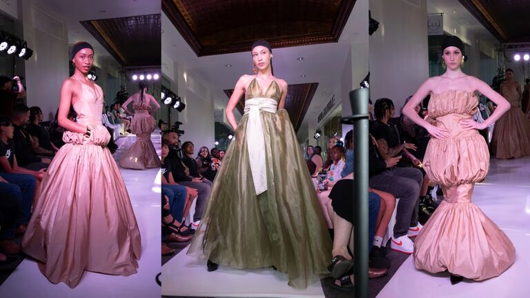 Three models walk the runway at a fashion show in various stylish dresses. The setting includes bright lighting and spectators seated along the catwalk.