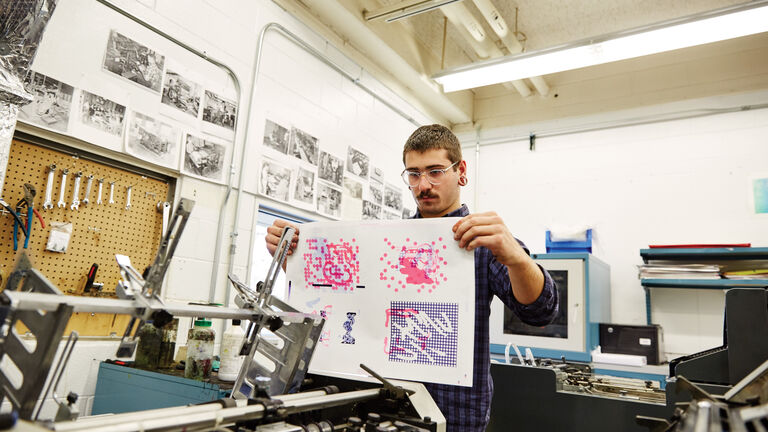A white man holding a print inside a printmaking facility