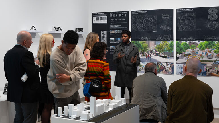 A gallery space filled with adults viewing and discussing the displayed artwork