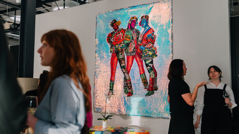 A photo of three people standing around a bright, colorful painting in a gallery.