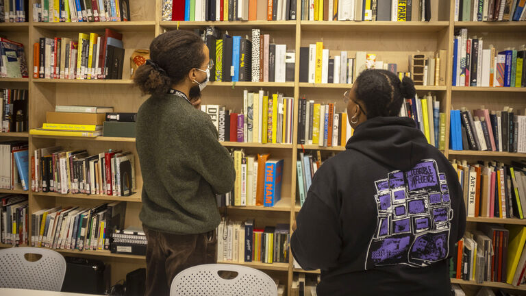 Two students looking at books on a shelf at the SAIC Library