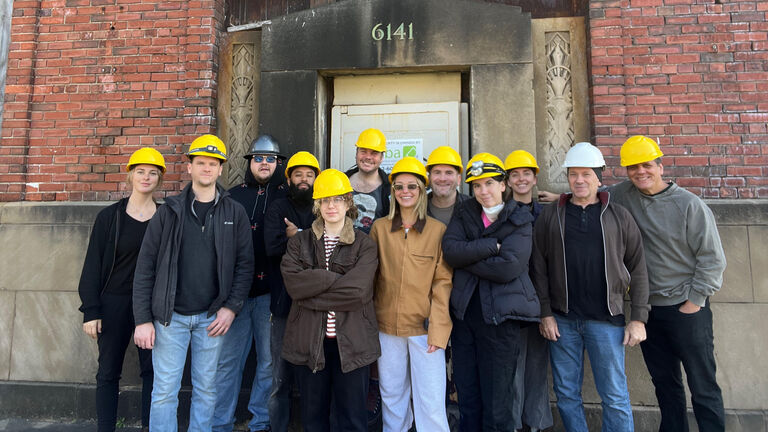 A group of students wearing yellow hard hats outside of a building