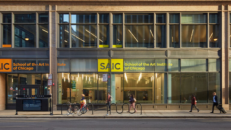 SAIC students walk in front of a campus building at sunset.