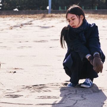 A picture of a person sitting down in the sand by a stick. 