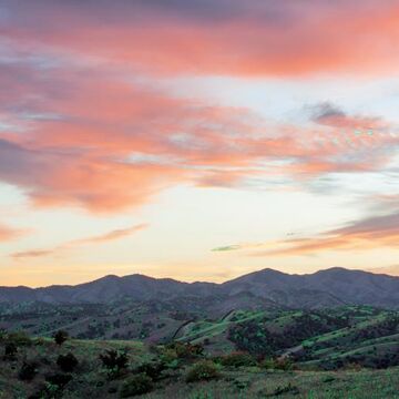 Mountains and a grassy hillside under a pink and orange sunset.