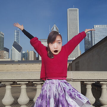 A person wears a mask of their own face in front of the chicago skyline