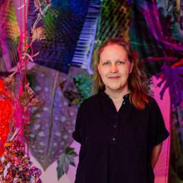 Aimee Beaubien wears a black shirt and stands in front of a multi-color jungle scene