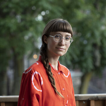 Kayla looks to the camera with a closed lipped smile, hair braided and resting on the right shoulder.