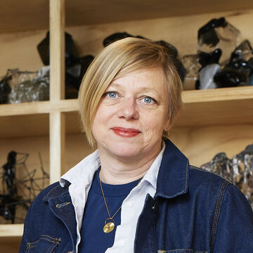 Christine wears layers that include denim jacket, white collared shirt and a blue tee.