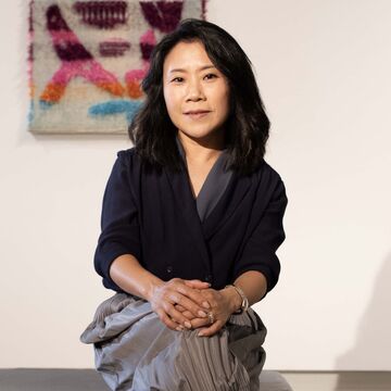 A photo of SAIC president Jiseon Lee Isbara sitting down in front of three works of art.