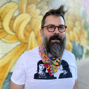 A white man with glasses in front of a bright mural