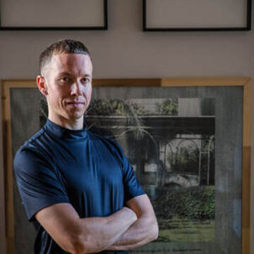 An arts administrator in a blue shirt poses in front of a painting