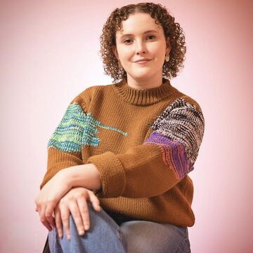 Portrait photo of Selena Wolfe sitting cross legged in front of a pink background