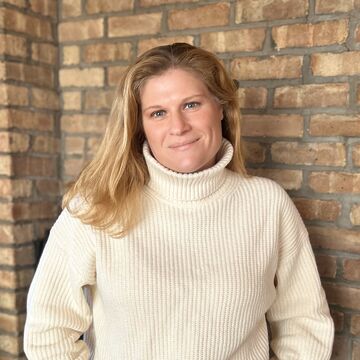 Headshot of an adult white woman smiling against a brick wall