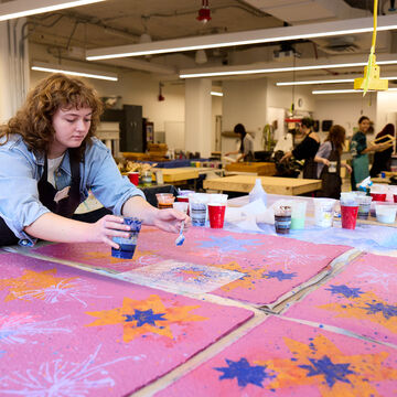 Student creating a paper making project in a studio environment with other students in the background 