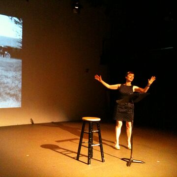 Holly Hughes, visiting artist and scholar, on stage in front of a screen.