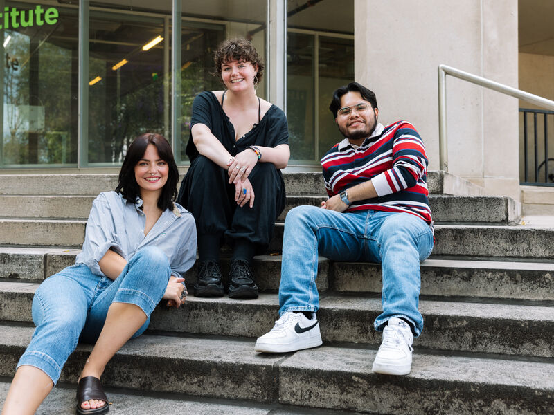 Three SAIC students smile as they sit on the steps of SAIC's campus.