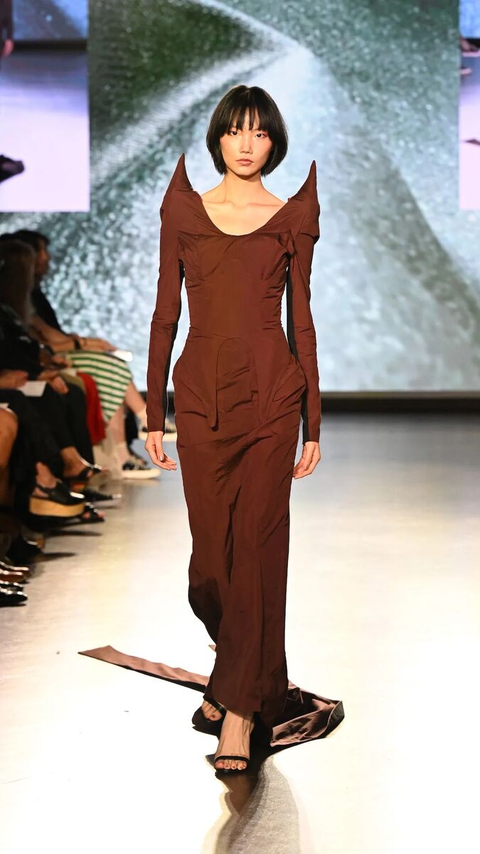 A model walks down a runway in a sculptural brown gown