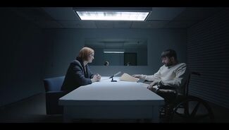 Still from a film of two people speaking to each other across a table 