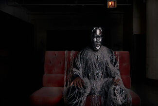 Image by Cecil McDonald, Jr. of a seated and masked subject, draped with strings of iridescent beads.