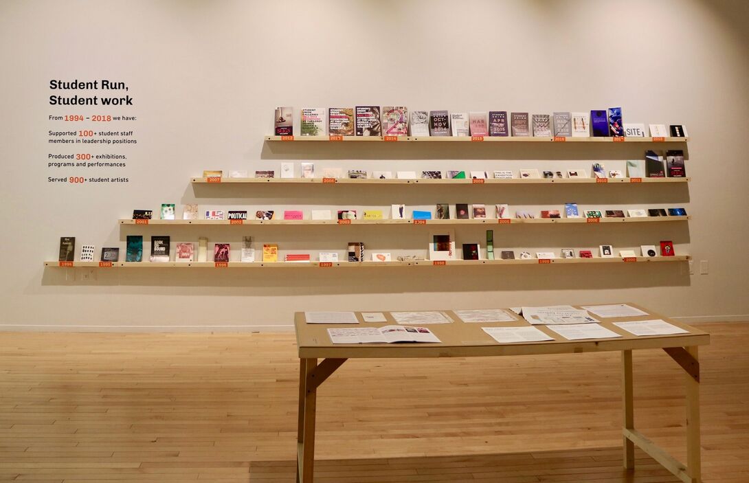 Four full bookshelves on the wall of a gallery.