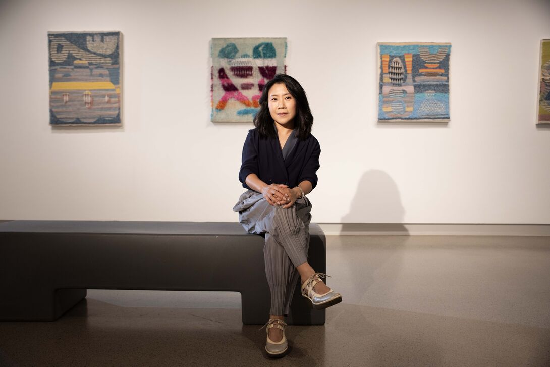 A photo of SAIC president Jiseon Lee Isbara sitting down in front of three works of art.