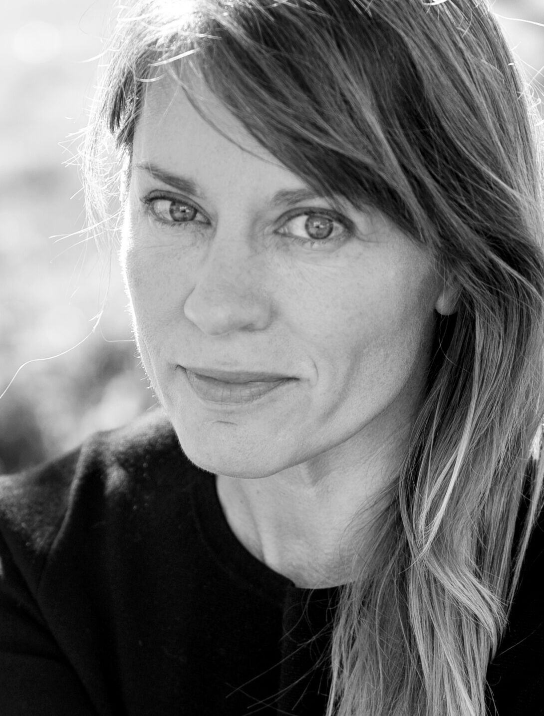 Black and white photo of a woman with long medium blonde hair and light eyes wearing a black shirt