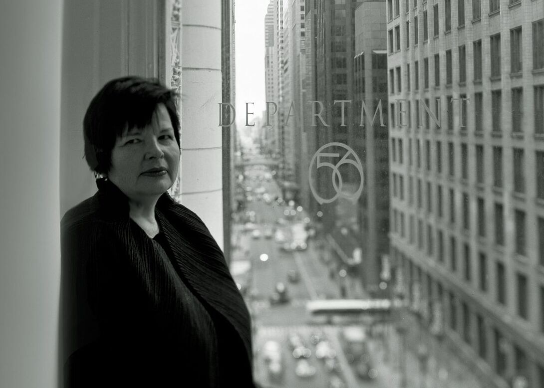A woman with short dark hair standing in front of a large window that faces a busy Chicago street