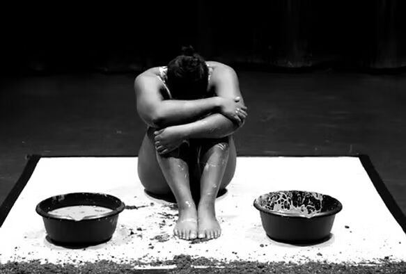  woman sitting on the floor, positioned next to two buckets of water, reflecting a moment of tranquility and focus.