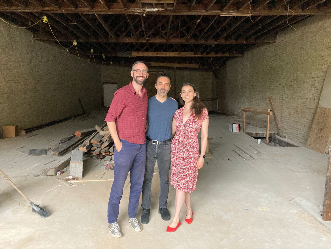 Three individuals stand in a cavernous space under construction